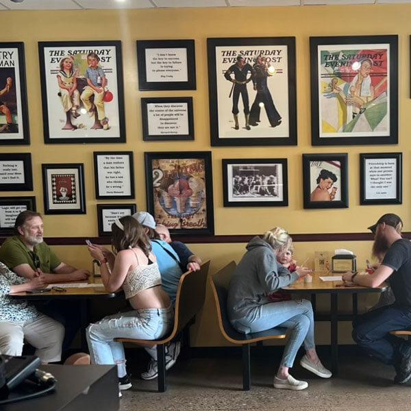 Inside Scoop Creamery interior — customers at tables beneath framed vintage Saturday Evening Post covers